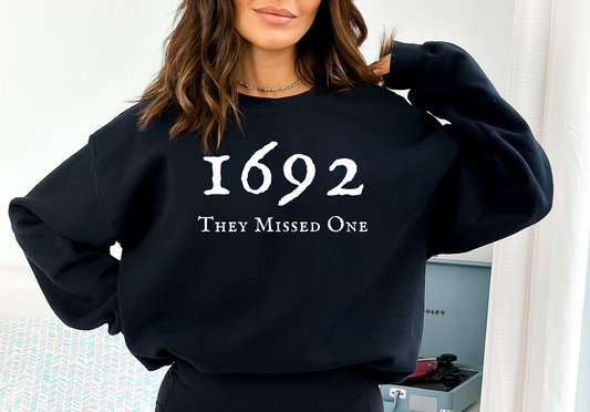 Woman wearing black crewneck sweatshirt that says 1692, they missed one. Halloween shirt about the Salem Witch Trials.
